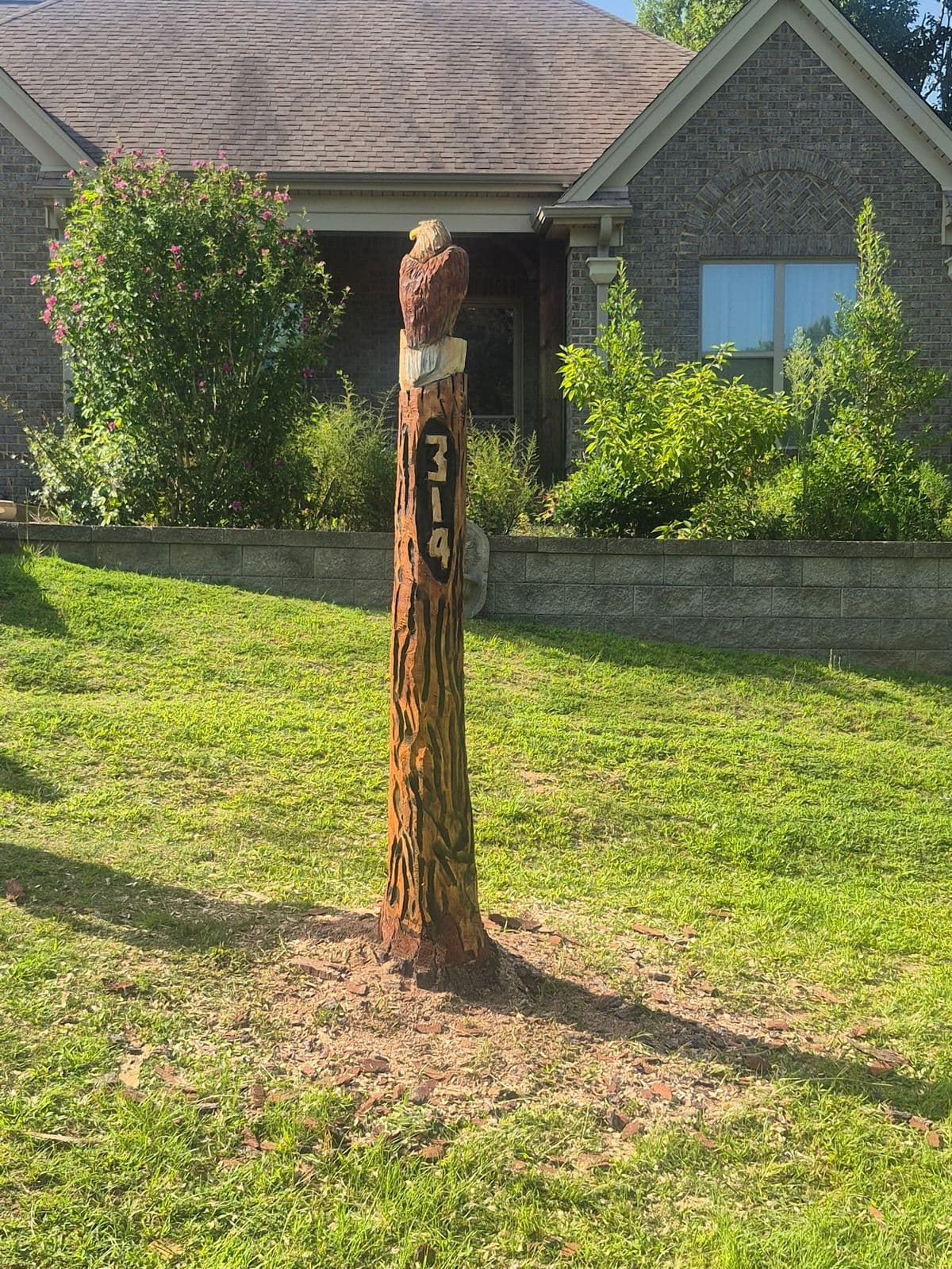 Slim trunk in a front lawn carved into a house-number post topped with an eagle