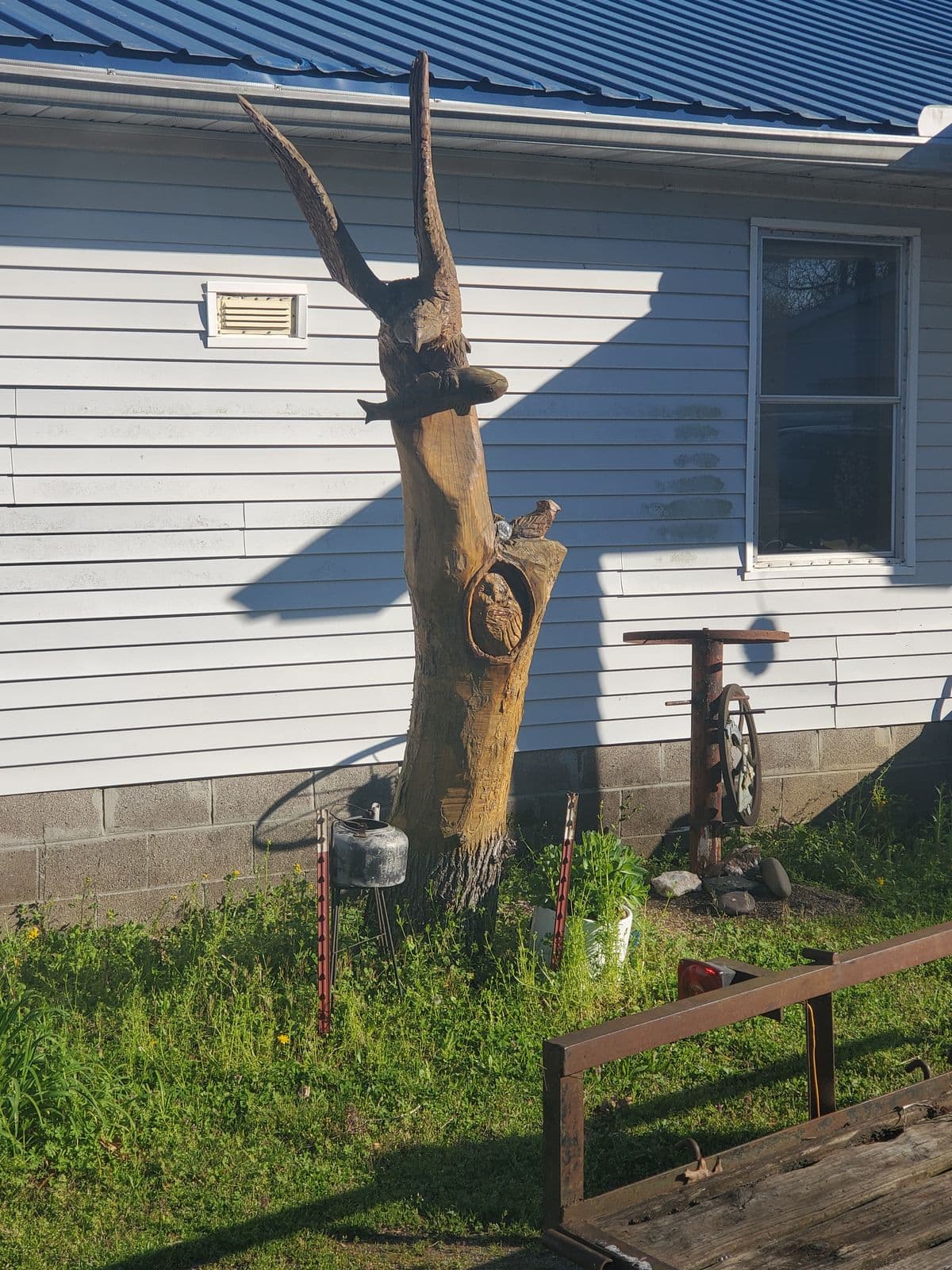Dead tree beside a house carved into a buck with tall antlers and an owl in a hollow