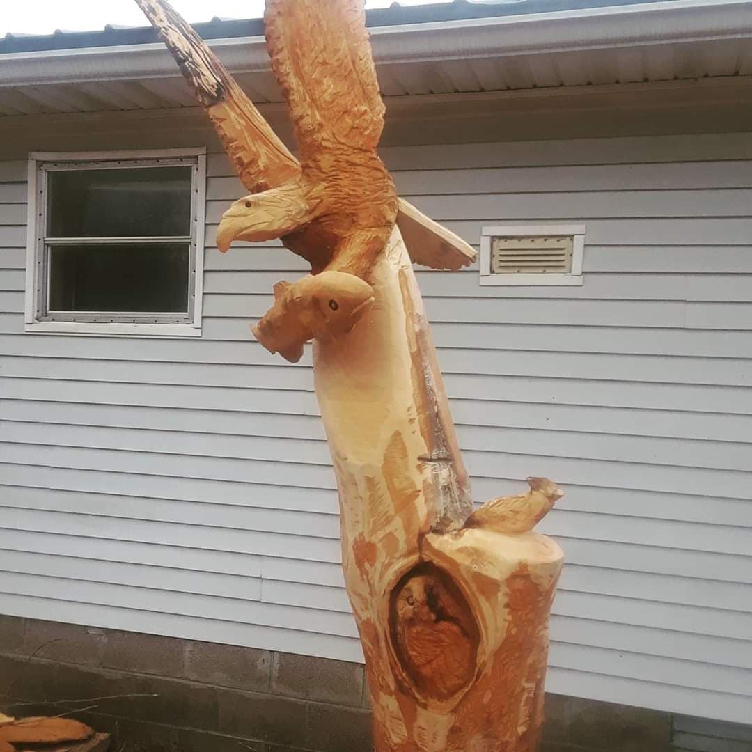 Tree trunk beside a house carved into a landing eagle with an owl tucked in a hollow below